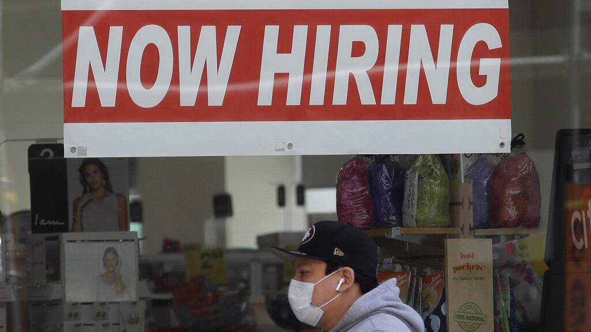ARCHIVO - Esta foto de archivo del 7 de mayo de 2020 muestra a un hombre con una mascarilla mientras camina bajo un cartel de "Estamos contratando" en una farmacia CVS durante el brote del coronavirus en San Francisco. El jueves 12 de noviembre, el número de personas que solicitaron beneficios de desempleo cayó la semana pasada a 709,000, la cuarta caída consecutiva y una señal de que el mercado laboral se está recuperando lentamente. Las cifras coinciden con un brusco resurgimiento de las infecciones víricas confirmadas hasta alcanzar un máximo histórico por encima de 120,000 al día. (AP Photo/Jeff Chiu, Archivo)