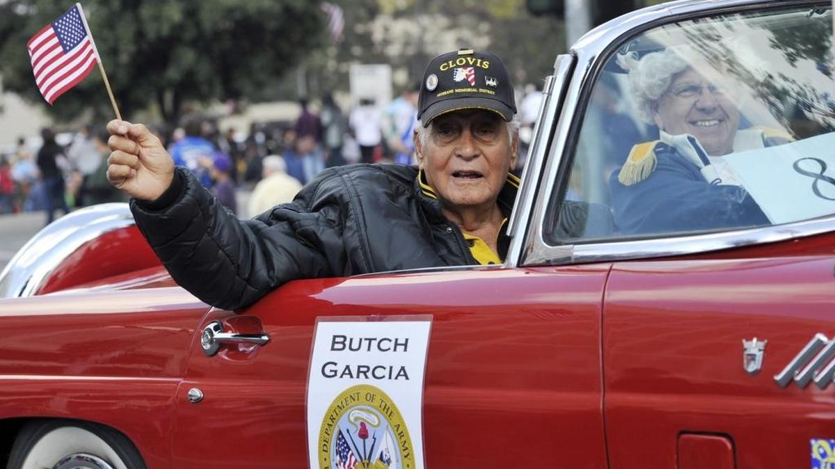 Korean War veteran Butch Garcia waves a flag during the 2015 Veteran’s Day Parade. This year’s grand marshal is Lt. Col. Oliver North.