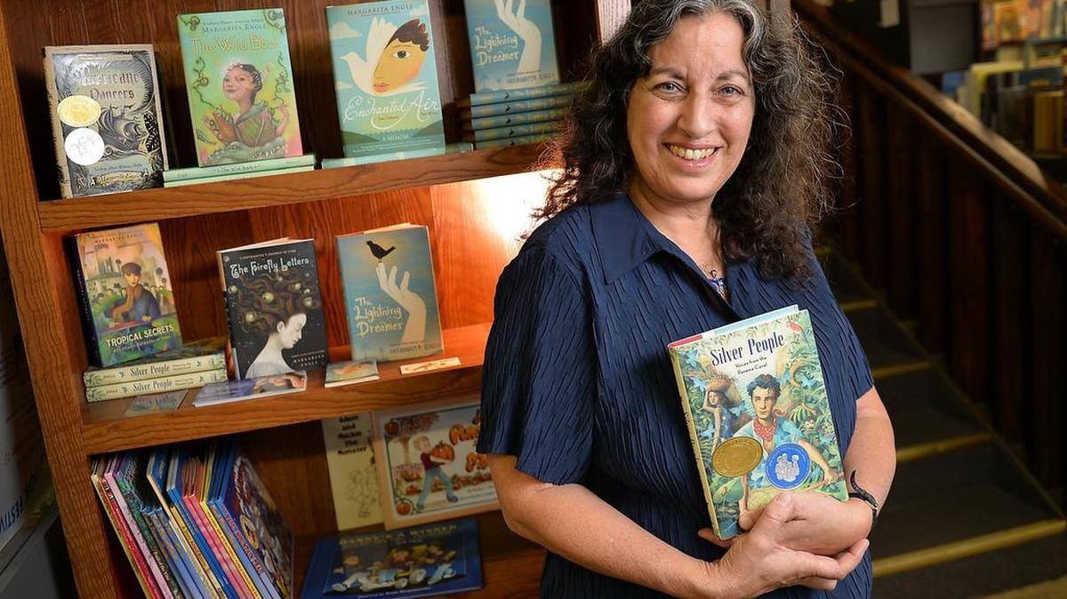 
Writer Margarita Engle, of Clovis, holds one of her books, “Silver People,” in front of a bookshelf filled with other books she has written. 
