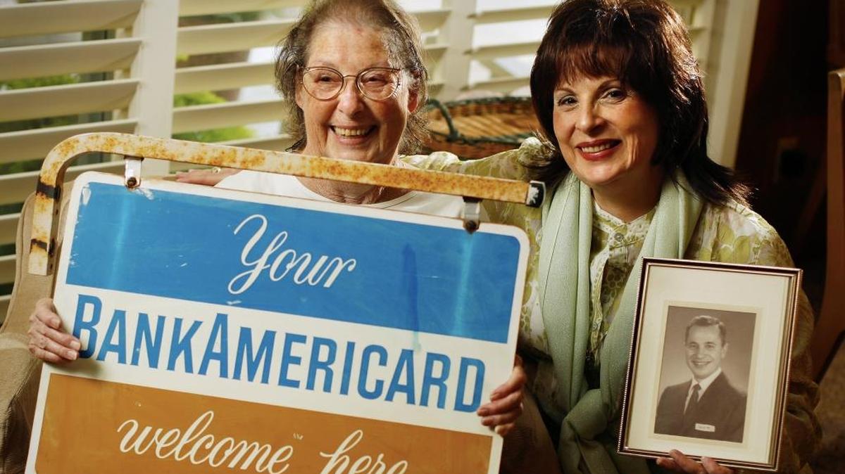 JoAnn Skoufis, right, holding a photo of her father Fred sits with her mother Dorothy Skoufis who holds an originial business sign for the BankAmericard, a credit card that pre-dates Visa and was test marketed in Fresno by the late Fred Skoufis of Bank of America. CRAIG KOHLRUSS/THE FRESNO BEE