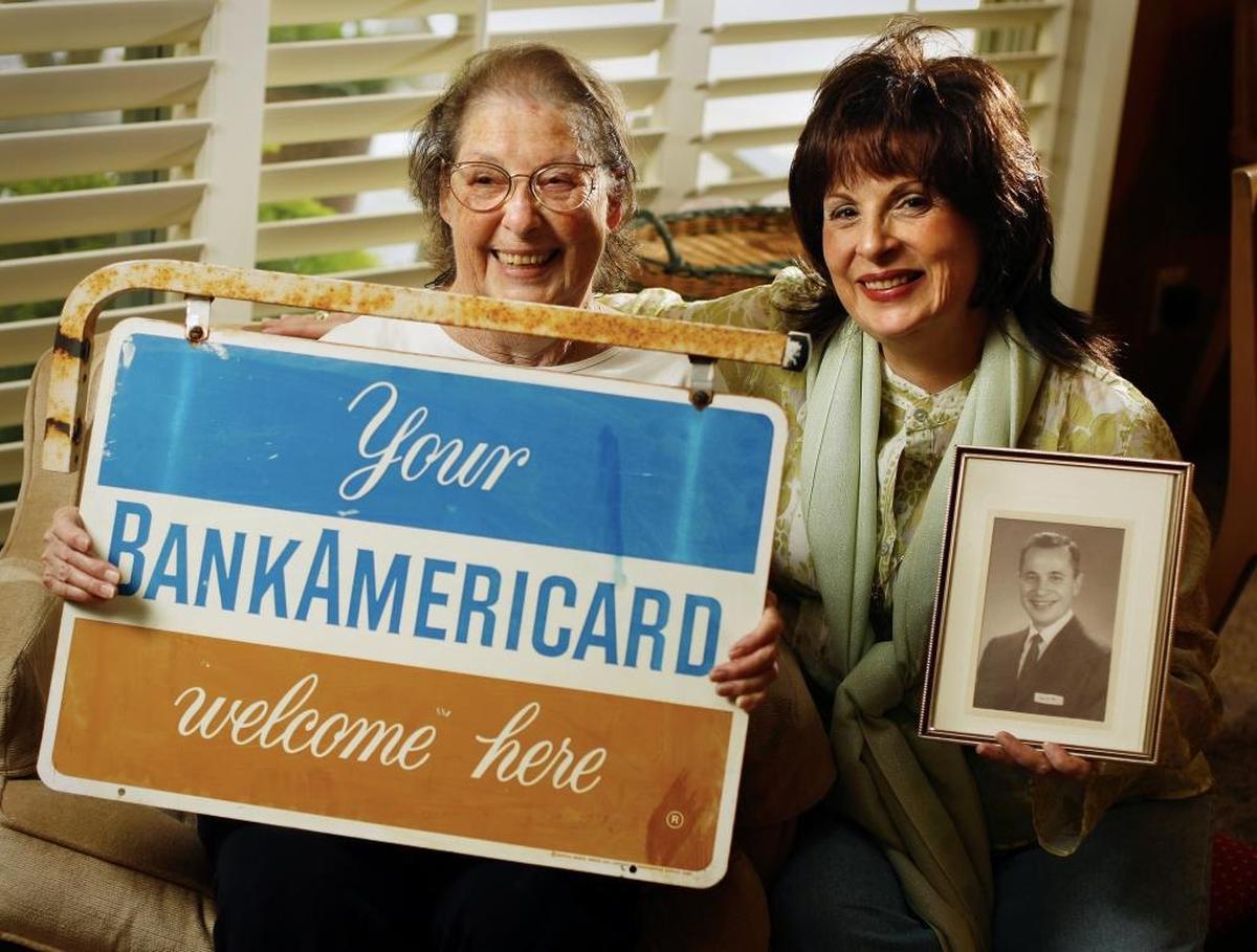 JoAnn Skoufis, right, holding a photo of her father Fred sits with her mother Dorothy Skoufis who holds an originial business sign for the BankAmericard, a credit card that pre-dates Visa and was test marketed in Fresno by the late Fred Skoufis of Bank of America.
