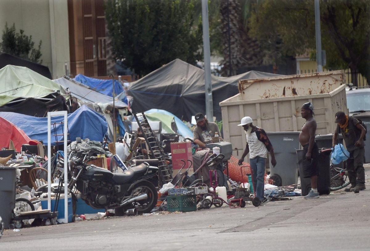 Homeless men hunt for salvageable items in piles along F Street, near Santa Clara Street and the Poverello House, Thursday, Aug. 20, 2020. Frustrated by the lack of safety on Santa Clara Street and the county’s inability to shelter more people, homeless advocate Dez Martinez started a safe homeless camp on her own.