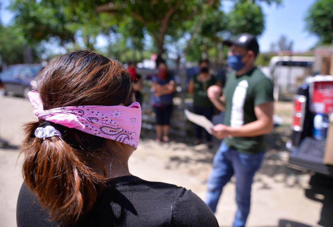 A woman wears a bandana mask as she and others listen to instructions for distrinution of food and needed wares including surgical masks to farmworkers Saturday afternoon, May 9, 2020 near Rolinda, CA.