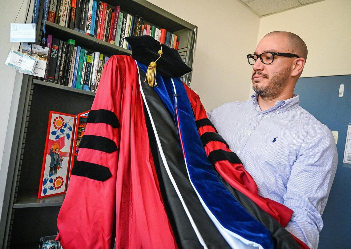 Everett A. Vieira III, an assistant professor in the political science department at Fresno State, holds up his academic regalia, which he will wear during upcoming graduation ceremonies, in his office on Tuesday, May 17, 2022.