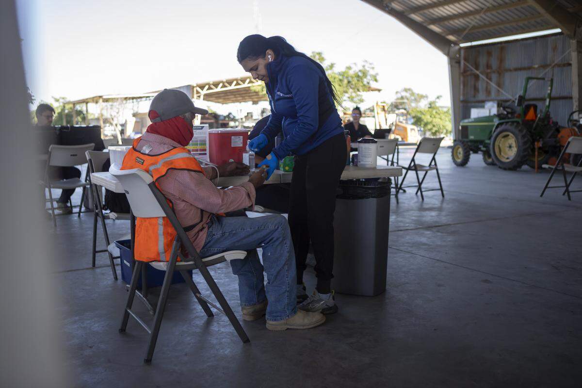 UCSF-Fresno staff member checks the blood sugar of a farmworker during a check-up in an equipment barn during a Rural Mobile Health program visit at a farm outside of Helm on June 16, 2025. Photo by Larry Valenzuela, CalMatters/CatchLight Local