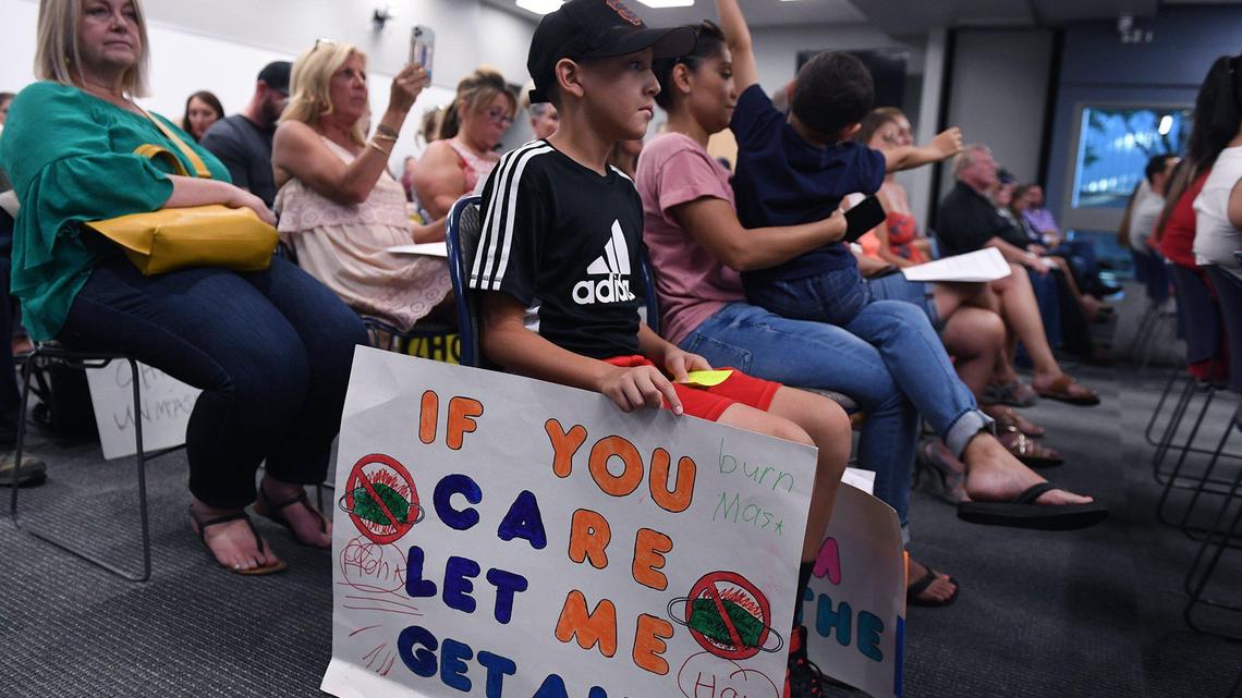 Austin Perez, 10, sits with his mother Vanessa Perez, holding Mason Parez, 5, with a sign against mask-wearing at the Clovis Unified School Board meeting Wednesday night, July 21, 2021 in Clovis
