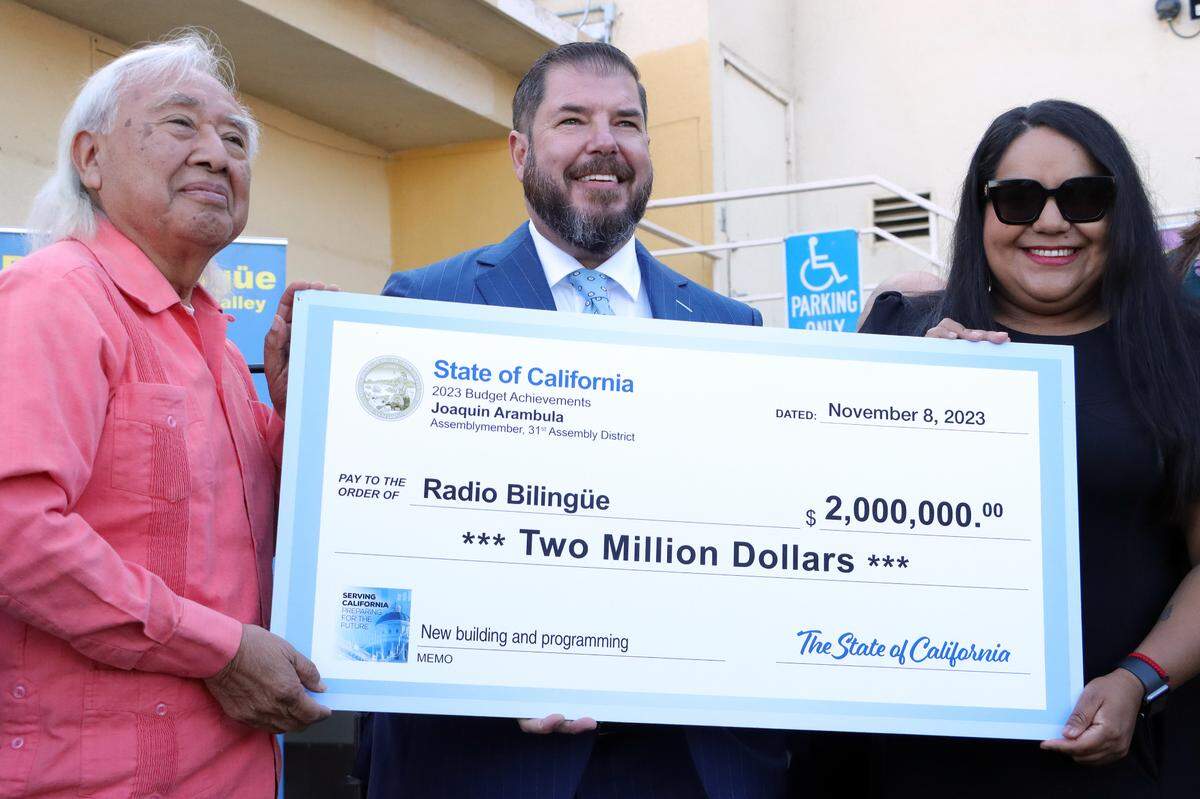 El fundador y director ejecutivo de Radio Bilingüe, Hugo Morales, acepta una asignación estatal de $2 millones de manos del asambleísta Joaquín Arámbula y de su directora de distrito, María Lemus, durante una ceremonia celebrada el 8 de noviembre de 2023 en las instalaciones de la emisora de radio, en el sureste de Fresno.