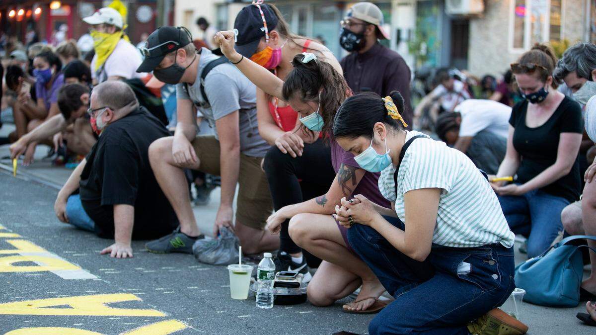 People bow in prayer as people such as Emmett Till and George Floyd are remembered, Tuesday, June 9, 2020, in Philadelphia. The neighborhood came together to paint “End Racism Now” and the names of victims. (Charles Fox/The Philadelphia Inquirer via AP)