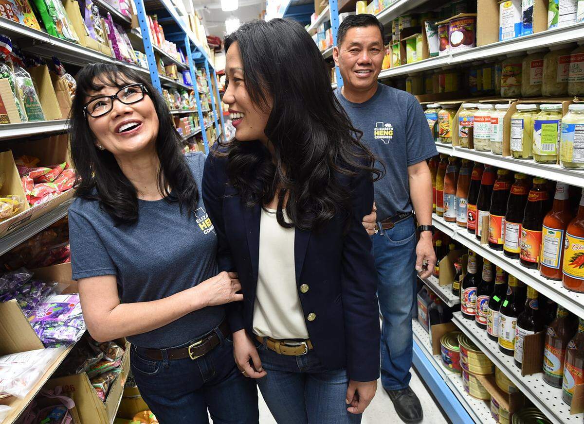 Siv Khoeu, left, revels in the congressional run by her daughter, Elizabeth Heng, center, with her husband, and Heng's father Chieu Heng, as they walk the aisle of the family's Rasmey Market, where Elizabeth worked as a child.