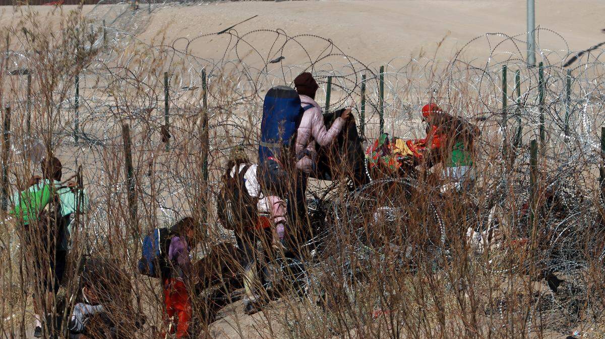 Migrantes intentan cruzar la cerca de alambres en la frontera que divide a México de los Estados Unidos, el 17 de enero de 2024, en Ciudad Juárez.