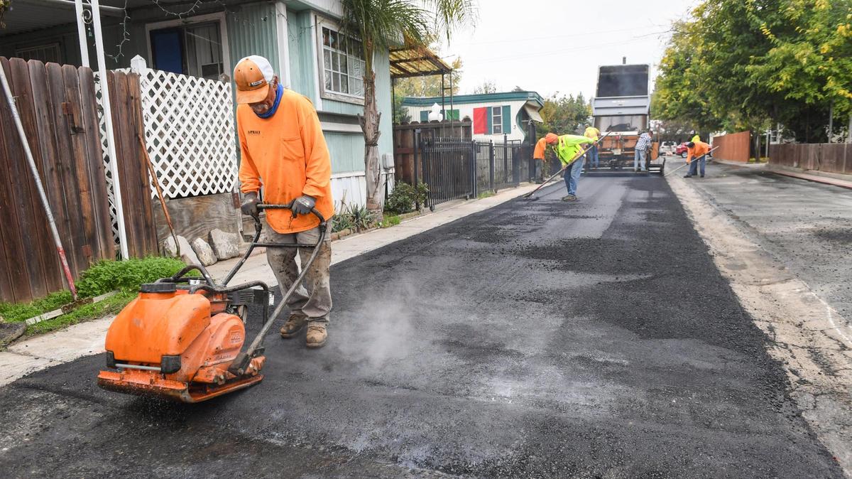 Workers put down new asphalt on the streets in the Trails End Mobile Home Park in Fresno on Tuesday, Nov. 16, 2021. For years the street were full of cracks and potholes that would fill with water and attract mosquitos. Fresno County Superior Court has appointed a receiver to remediate the troubled park and bring it under code compliance.