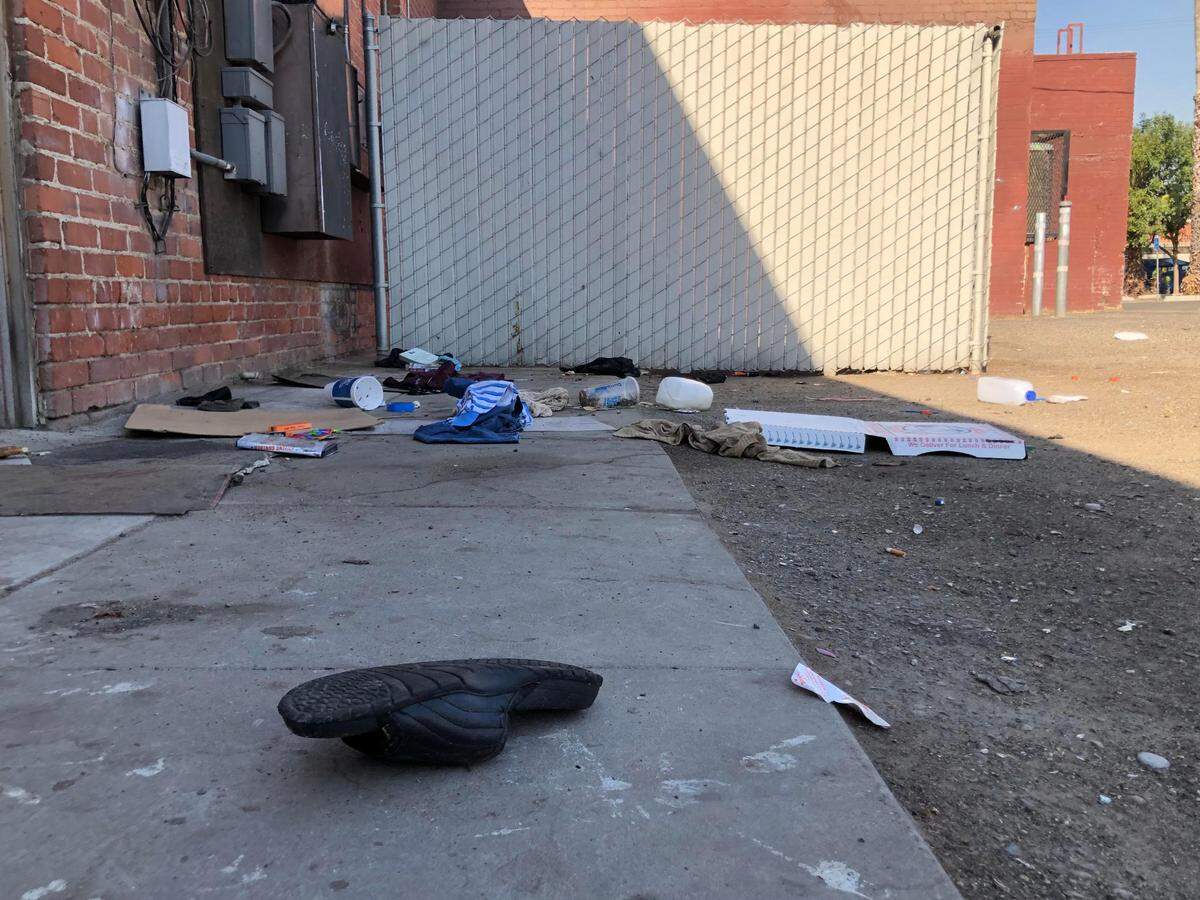 A single shoe, articles of clothing, and pieces of cardboard are found behind Livingstone’s Restaurant and Pub in Fresno’s Tower district on Thursday, Sep. 8, 2022. Unhoused individuals often gather in the shade near dumpsters behind the restaurant.