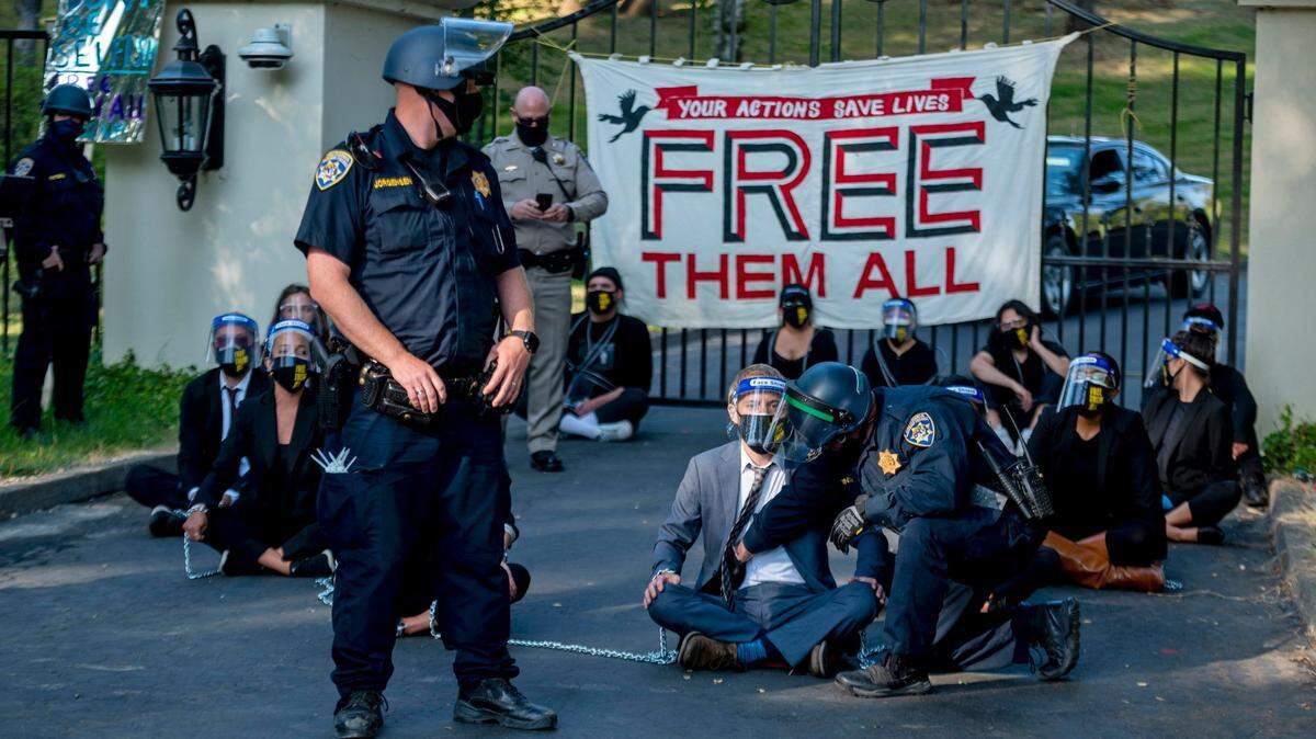FILE - In this July 27, 2020, file photo, a California Highway Patrol officer inspects a chained protester who was part of a group calling for mass prison inmate releases outside of California Gov. Gavin Newsom’s mansion in Fair Oaks, Calif. California state prison officials say in a recent court filing that as many as 17,600 inmates are eligible for release due to the coronavirus, 70% more than previously estimated and a total that victims and police say includes dangerous criminals who should stay locked up. (Daniel Kim/The Sacramento Bee via AP, File)