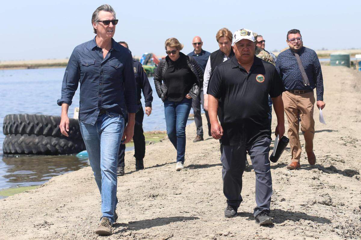 California Gov. Gavin Newsom, far left, along with Kings County Supervisor Richard Valle, center, and Tulare County Supervisor Eddie Valero, far right, and other state officials.&nbsp;arrive to speak to the media at Hansen Ranches on 6th Avenue Tuesday, April 25, 2023, south of Corcoran, CA.