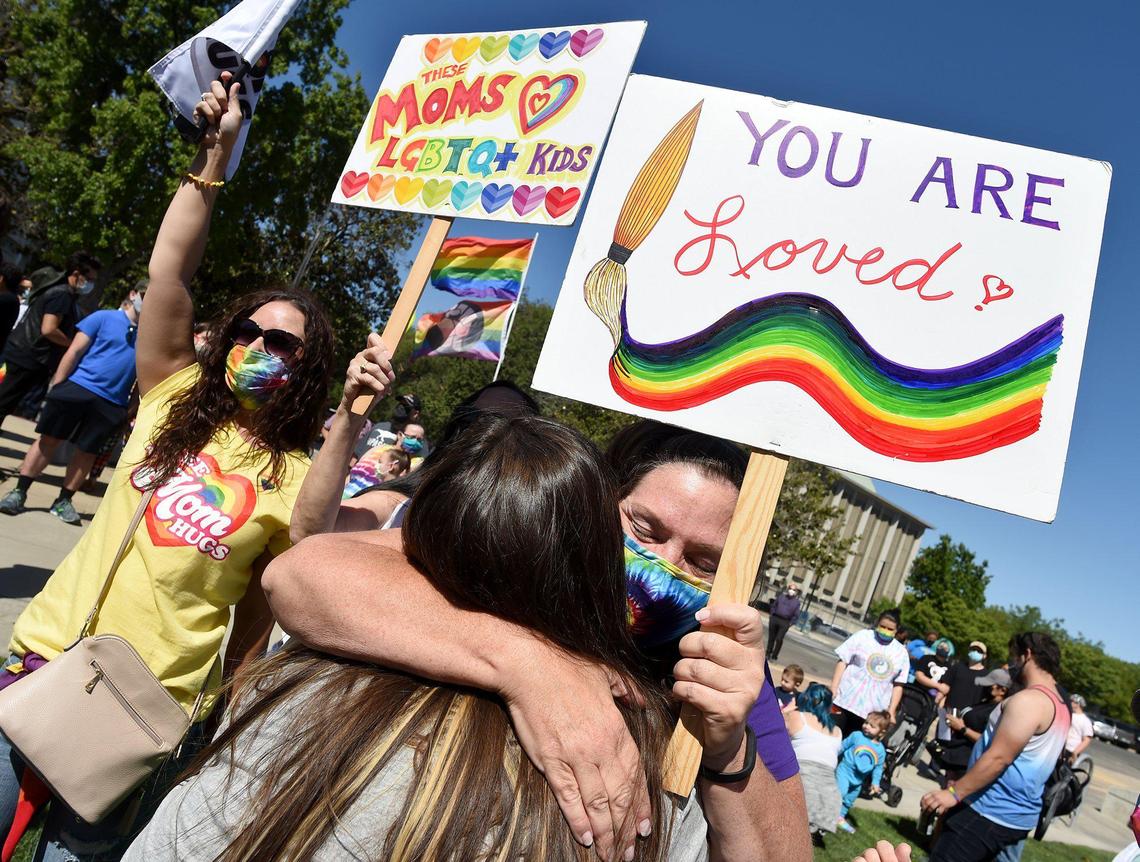 Shelly Mast, with sign, hugs friend Carmen Gutierrez, during the Pride Flag Raising Ceremony at City Hall, Friday June 11, 2021.