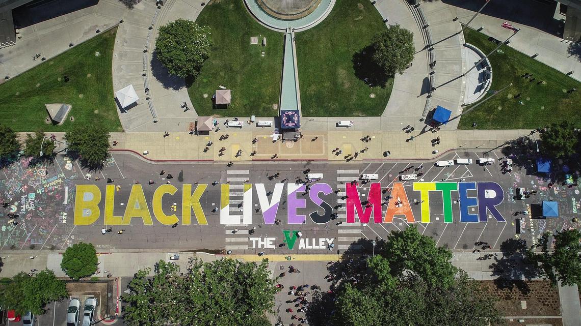 Volunteers work on painting a Black Lives Matter street mural during the BLM street art event on P Street in front of Fresno City Hall on Thursday,