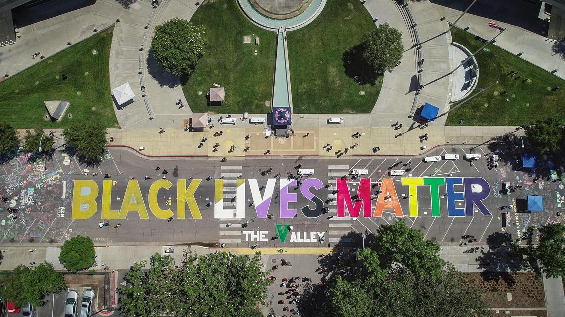 Volunteers work on painting a Black Lives Matter street mural during the BLM street art event on P Street in front of Fresno City Hall on Thursday,
