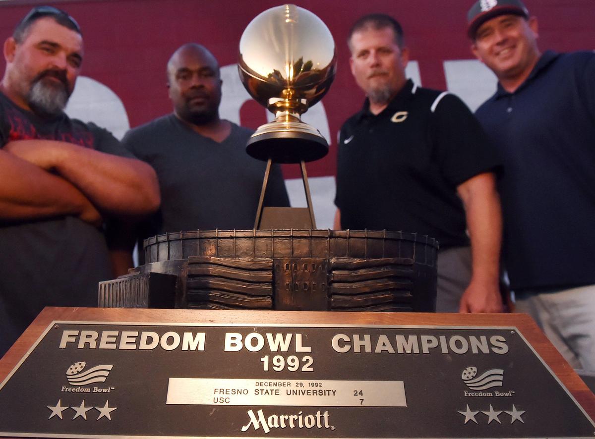 Members of the 1992 Fresno State team from left nose guard Zack Rix; safety Johnny Johnson; right tackle Jesse Hardwick; and right guard Rus Hartmann gather around the 1992 Freedom Bowl trophy earned with a win over USC.