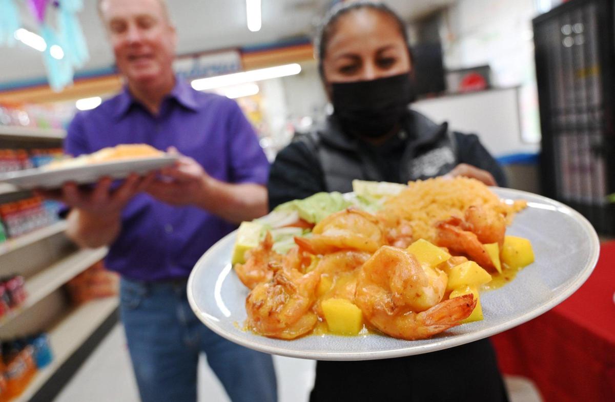 Qué pasó Camarón? co-owner Mireya Ramirez, right, holds forth the popular Mangonero Shrimp special which her husband Miguel Castro created, while public relations manager Don Rotella stands in the background Thursday, April 14, 2022 in Fresno. Qué pasó Camarón? is located inside and at the back of El Toro Loco Market, offering Mexican food for dine-in or takeout near Shields and West avenues.