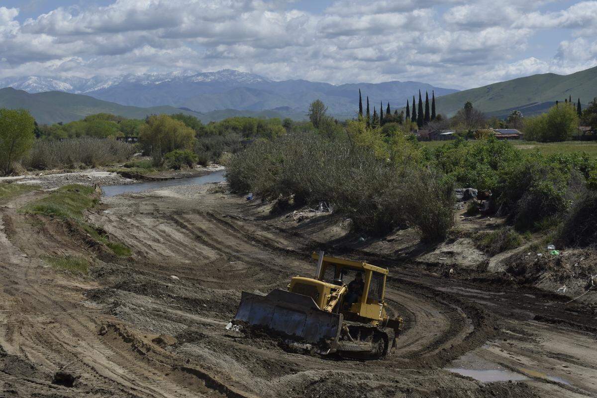 Bulldozers widen the Tule River channel in Porterville on April 4, 2023. With the snow-packed Sierra Nevada in the background, the machinery was working a few feet away from encampments of unhoused individuals – who survived recent floods – and live by the river.