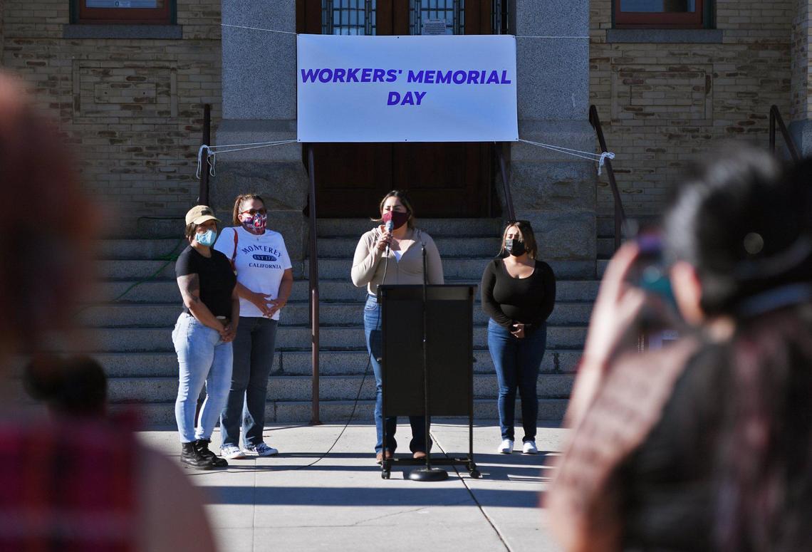 Alisa Flores, center, speaks with a microphone as she stands with others from Tulare Lideres Campesinas during an event on the steps of the old Kings County Courthouse in observance of essential workers who died from COVID-19 last year on Wednesday, April 28, 2021.