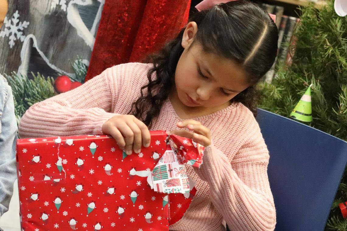 Ariana Ayala, de 8 años, de segundo grado, abre un regalo de Santa Clos durante el evento de Navidad de la Familia Migrante 2023 que se llevó a cabo en la biblioteca de la Firebaugh High School el 13 de diciembre.