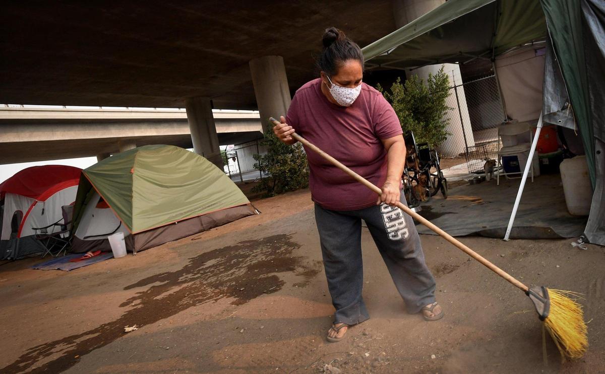 Rose Juarez DeLeon tidies up around her home, a tent under Highway 41, in a homeless encampment named the Dream Camp by residents, Thursday, Aug. 20, 2020. Fresno homeless advocate Dez Martinez set up the camp with community donations and help. She was frustrated by the lack of safety on Santa Clara Street, where hundreds of homeless individuals have set up camp, where the city has not picked up trash for months, and crime is growing.