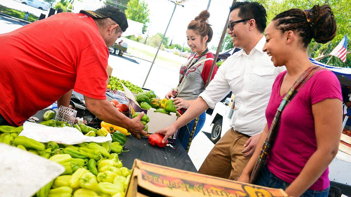 Fresno State students, from right, Rose Cardoso, Anoy Phuangsavath and Shoua Chang receive vegetables from a vendor at the Manchester Center Farmers Market Friday, July 18, 2014. The students are part of the Fresno State Food Recovery Network which recovers unwanted foods from vendors at the farmers market.