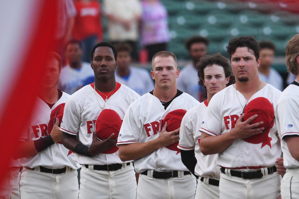 The Fresno Grizzlies watch as the color guard carries the American flag off the field at the start of the season opener against the Stockton Ports Friday, April 8, 2022 at Chukchansi Park in Fresno.