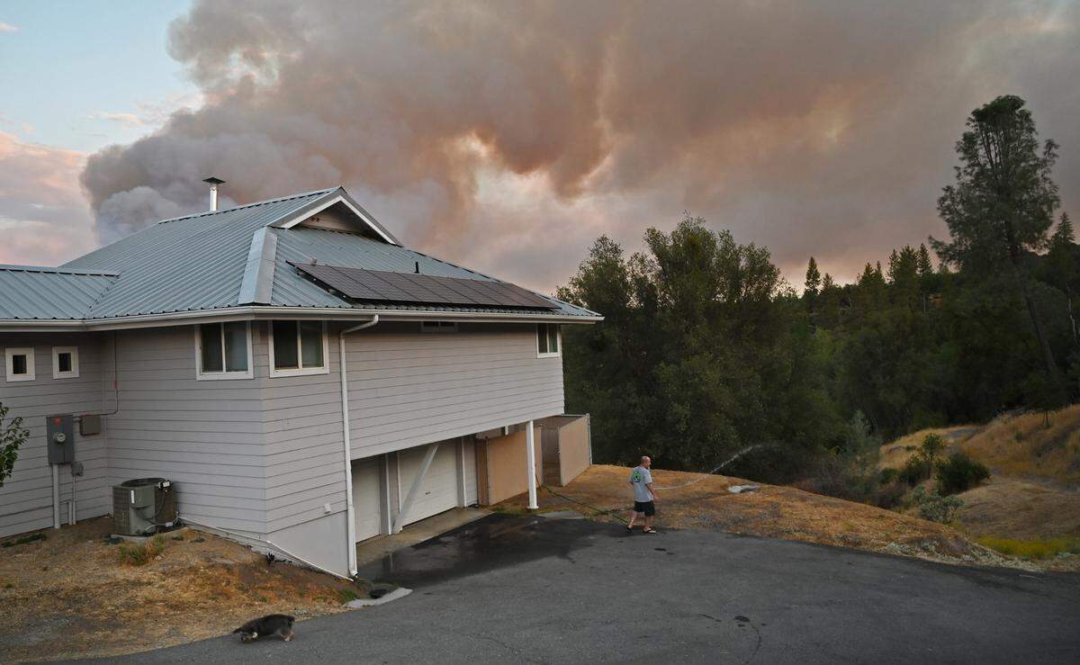 Joey Maxfield waters his house and yard after hearing of the Fork Fire, seen in the background, on Wednesday, Sept. 7, 2022.
