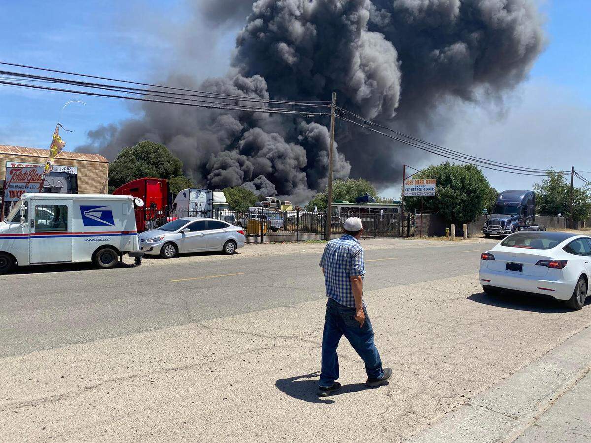 A passerby watches a fire at Fresno Foreign Wrecking on Thursday, May 19, 2022.