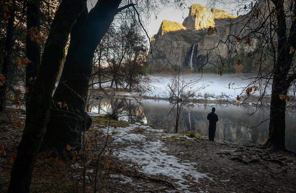A photographer sets up his camera in front of the Merced River with Bridalveil Fall in the distance as snow, ice and fog surround the area after storms moved through Yosemite National Park over the past few days, on Monday, Dec. 9, 2019.
