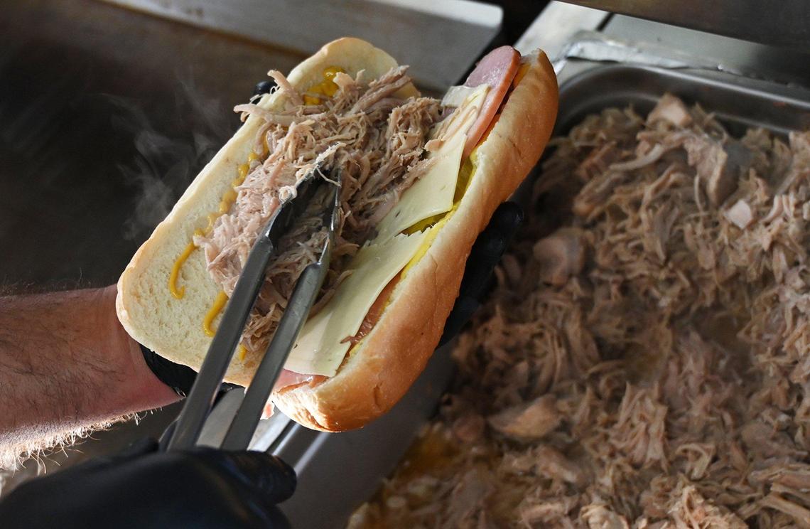 Lazaro Santana places pork as he creates a Cuban sandwich with Swiss cheese and ham Wednesday, March 16, 2022 in Fresno. Lazaro and his wife Niermin Santana have opened a food truck specializing in Cuban food.