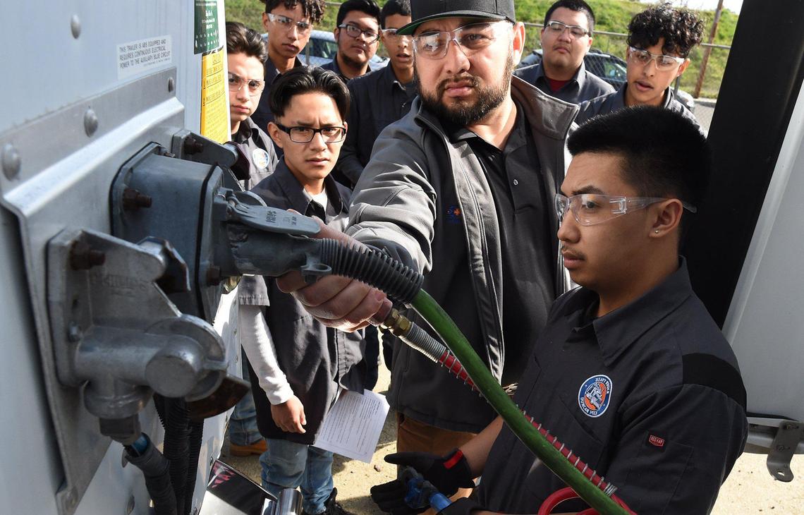 Eric Rubio, Diesel Truck Instructor in Duncan Polytechnical High School’s Heavy Duty Truck pathway program, center, shows students hydraulic cables connecting a truck to a trailer, including junior Asaya Kala, right.