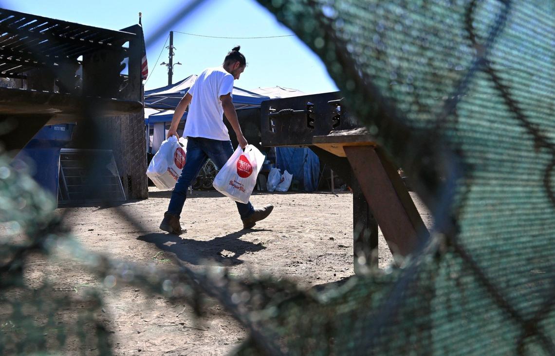 A man carries Grocery Outlet bags to a tent as we look inside the City of Tulare’s temporary encampment located at the south end of town Tuesday, Sept. 10, 2024.
