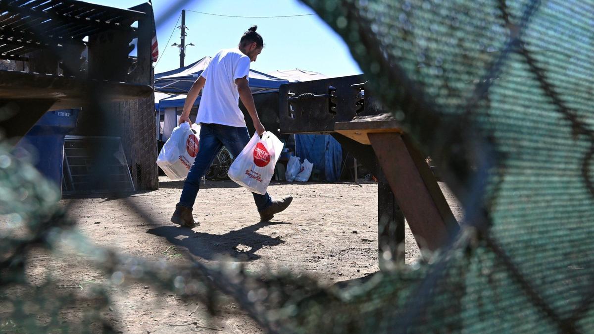 A man carries Grocery Outlet bags to a tent as we look inside the City of Tulare’s temporary encampment located at the south end of town Tuesday, Sept. 10, 2024.