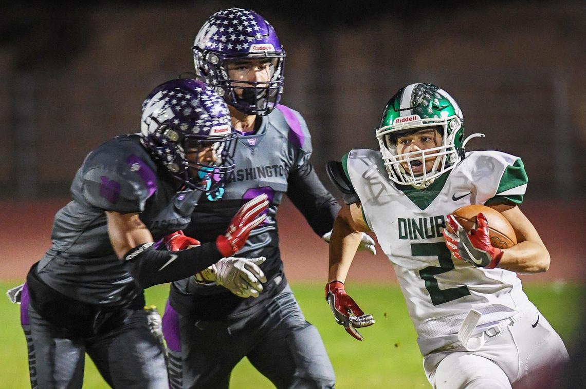 Dinuba’s Mikey Olivera, right, tries to get by Washington Union’s EJ Sotelo, left, and Herbert Denny on a run in their Central Section Division II playoff game at Jesse Ventura Stadium in Easton on Friday, Nov. 4, 2022.
