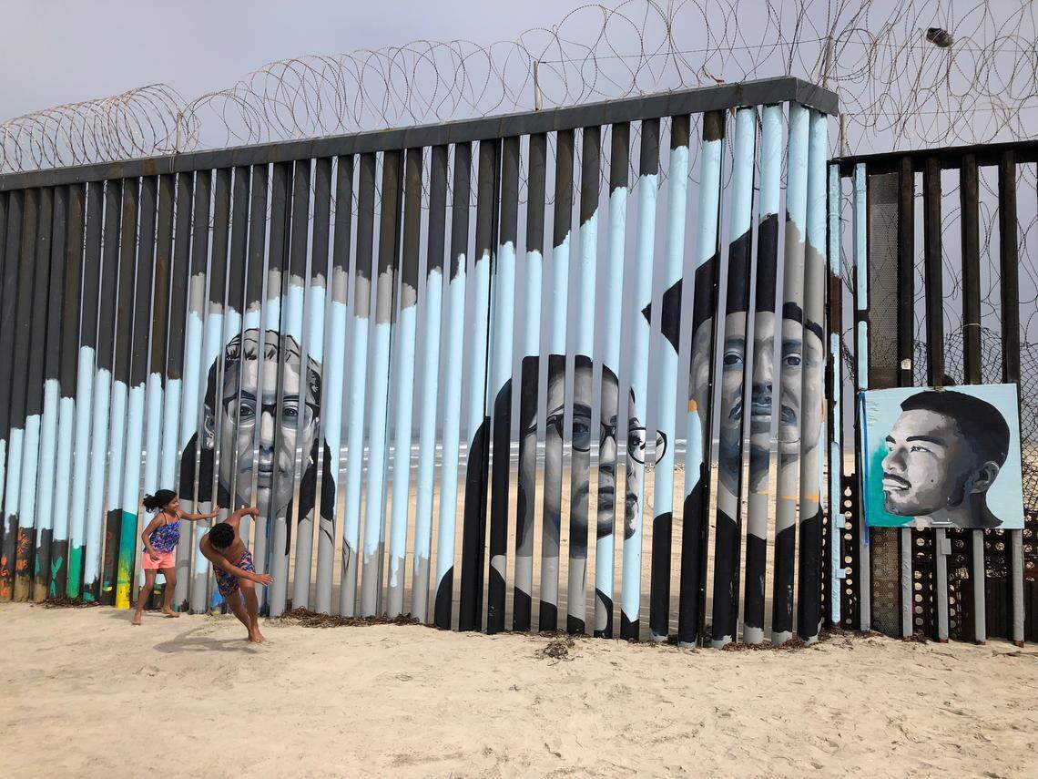 Children play in front of a new mural on the Mexican side of a border wall in Tijuana, Mexico Friday, Aug. 9, 2019. The mural shows faces of people deported from the U.S. with barcodes that activate first-person narratives on visitors’ phones. Lizbeth De La Cruz Santana conceived the interactive mural in Tijuana as part of doctoral dissertation at the University of California, Davis. (AP Photo/Elliot Spagat)