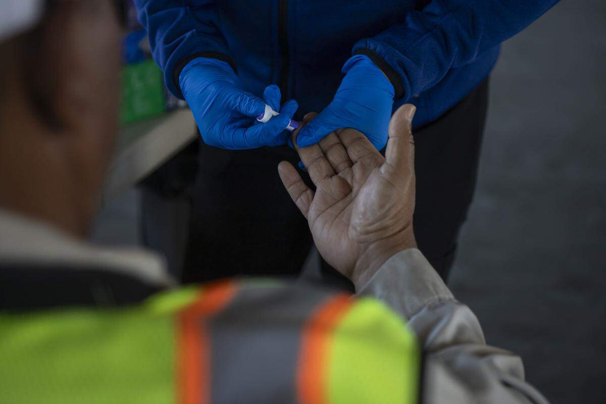 UCSF-Fresno staff member checks the blood sugar of a farmworker during a check-up in an equipment barn during a Rural Mobile Health program visit at a farm outside of Helm on June 16, 2025. Photo by Larry Valenzuela, CalMatters/CatchLight Local