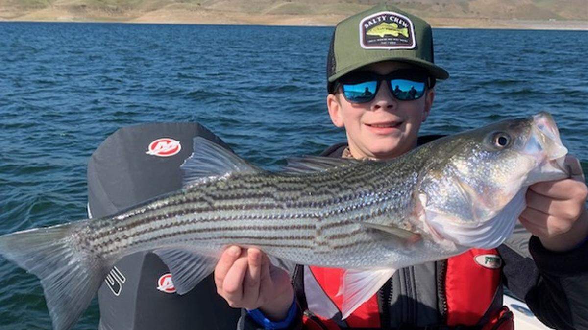 Thirteen-year-old Michael Weber of Fresno shows off his personal-best 24-inch striper caught on a trip Friday at San Luis Reservoir with his father, Scott Weber, and guide Roger George.