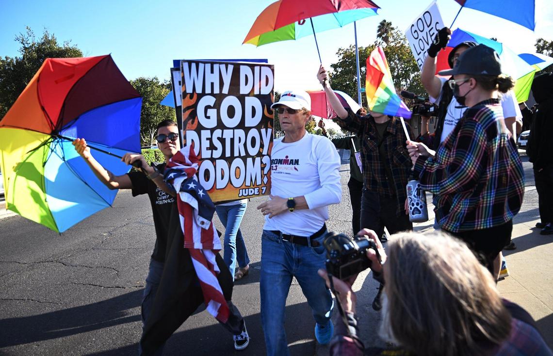 A member of a group representing Westboro Baptist Church, center, is followed by a coalition of LGBTQ+ organizations and supporters using Pride-themed umbrellas as shields in a counter-protest outside Roosevelt Hgh School Monday, Oct. 28, 2024, Fresno.