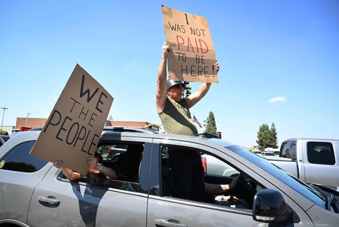 Sanger’s Rudy Rangel stands inside a passing car holding a sign as he passes the corner of Shaw and Clovis avenues for a Hands Off rally Saturday, April 19, 2025 in Clovis.