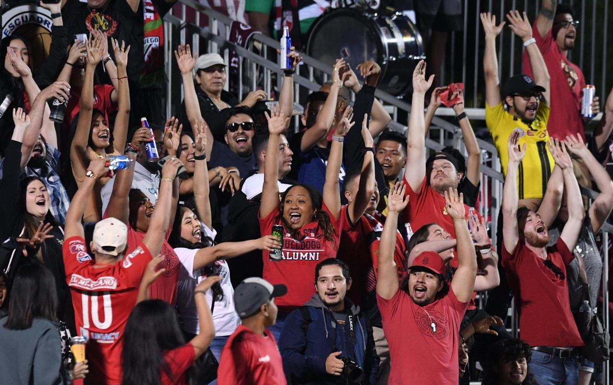 Central Valley Fuego FC fans raise their arms as The Wave continues circling through the stands in the home opener against Greenville Triumph SC to a final score of 1-1 Saturday night, May 7, 2022 in Fresno.