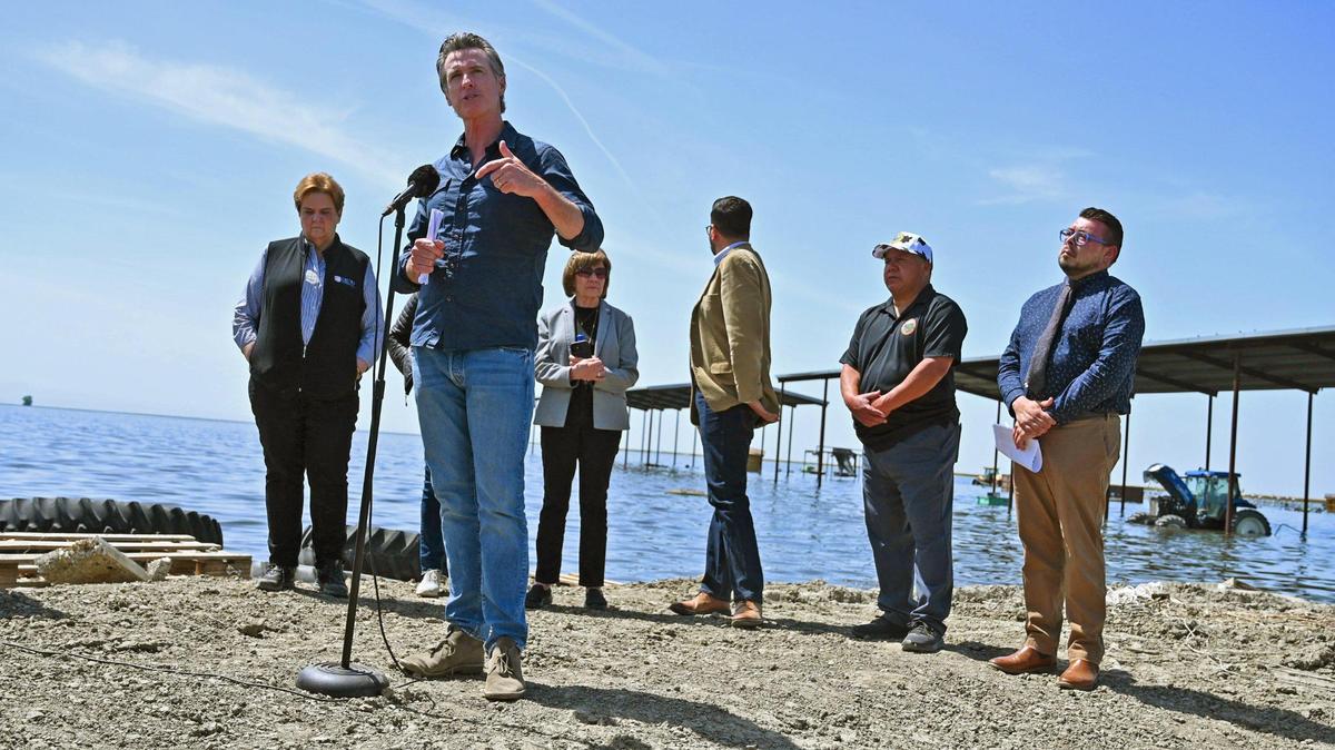 California Gov. Gavin Newsom, second from left, speaks near Corcoran, in an area surrounded by flooded land last month. After big investments in climate last year, Newsom is scaling back on environment protections due to California’s billion dollar budget shortfall.
