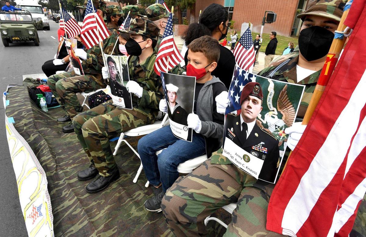 Donning white gloves, young men and boys hold portraits of the 13 American service members killed in a bomb attack in Kabul last summer, honoring them on the Young Marines float during the Central Valley Veterans Day Parade, Thursday Nov. 11, 2021.