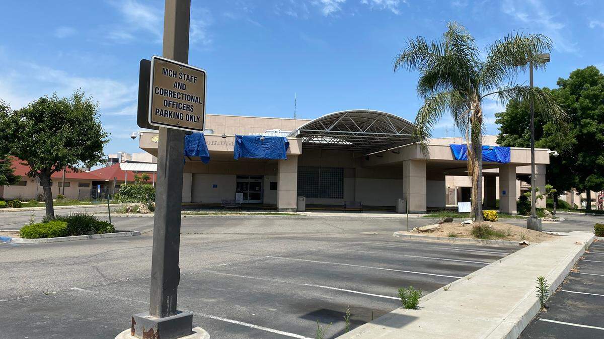 An empty parking lot with cracked pavement, faded stripes and weeds popping up are evident at the closed Madera Community Hospital, with blue tarps covering where the facility’s name was formerly displayed, on Tuesday, May 16, 2023. The hospital closed in January, but efforts are ongoing to explore ways to reopen it.