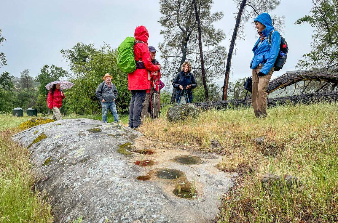 Hikers stop to talk about grinding holes during a hike to the top of the volcanic table mountain of the McKenzie Table Mountain Preserve through the Sierra Foothill Conservancy on Sunday, April 14, 2024.