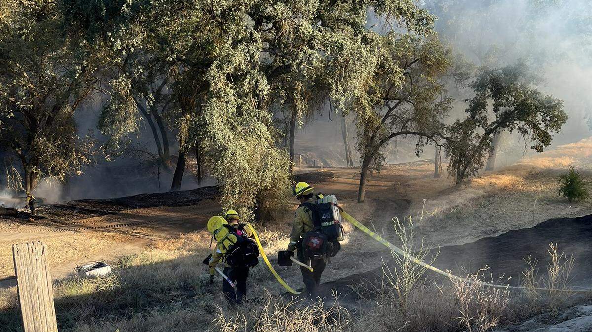 Firefighters lug hoses and hand tools as they hike into the Wahtoke Creek streambed north of Reedley to fight a vegetation fire on Saturday, July 2, 2022. The Reed incident was reported fully contained on Sunday morning, limiting the fire to 11 acres.