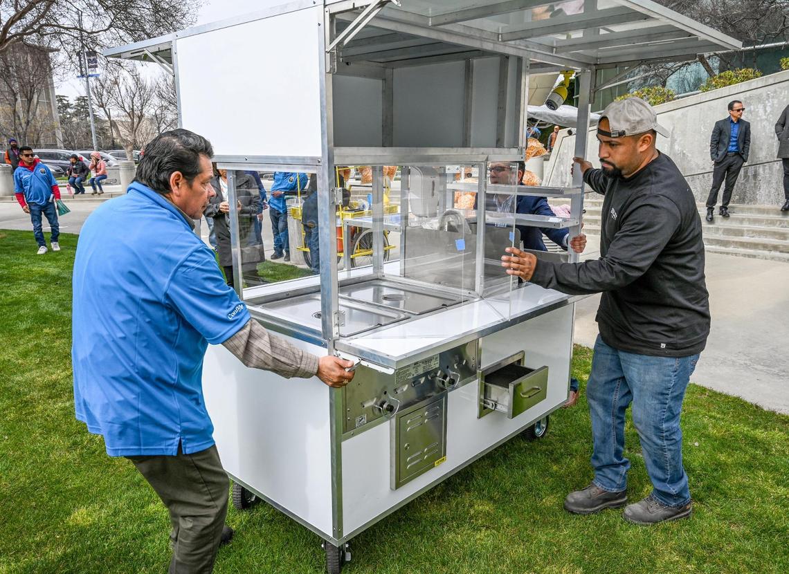 Orlando Gonzalez, right, of Cali Food Truck & Trailer Corp. gets help from a food vendor in pushing a new food cart prototype that Gonzalez’s company produced and meets permitting standards of the Fresno County Health Department during an unveiling event at Fresno City Hall on Thursday, March 9, 2023.