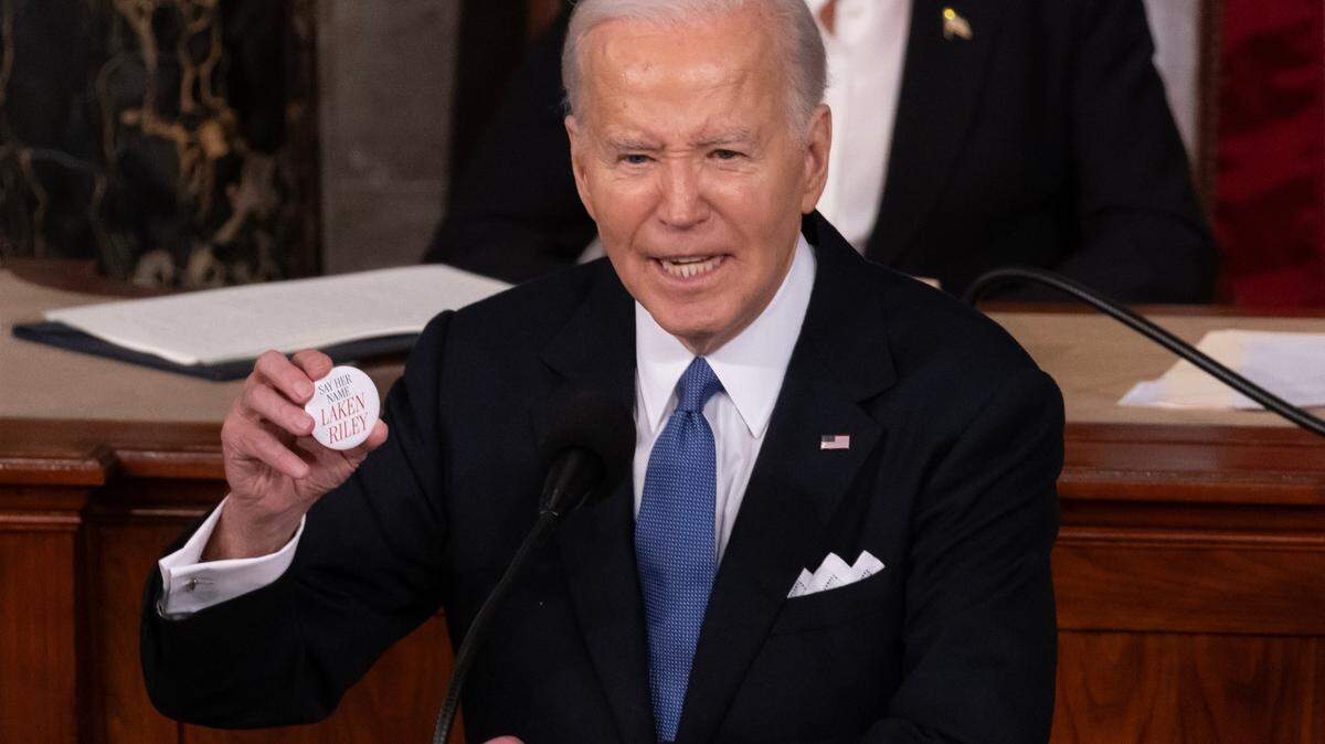 El presidente Joe Biden sostiene un pin que hace referencia al estudiante asesinado de Georgia, Laken Riley, mientras pronuncia su discurso sobre el Estado de la Unión ante una sesión conjunta del Congreso en marzo de 2024. / President Joe Biden holds a pin referring to slain Georgia student Laken Riley while delivering his State of the Union address before a joint session of Congress in March 2024.